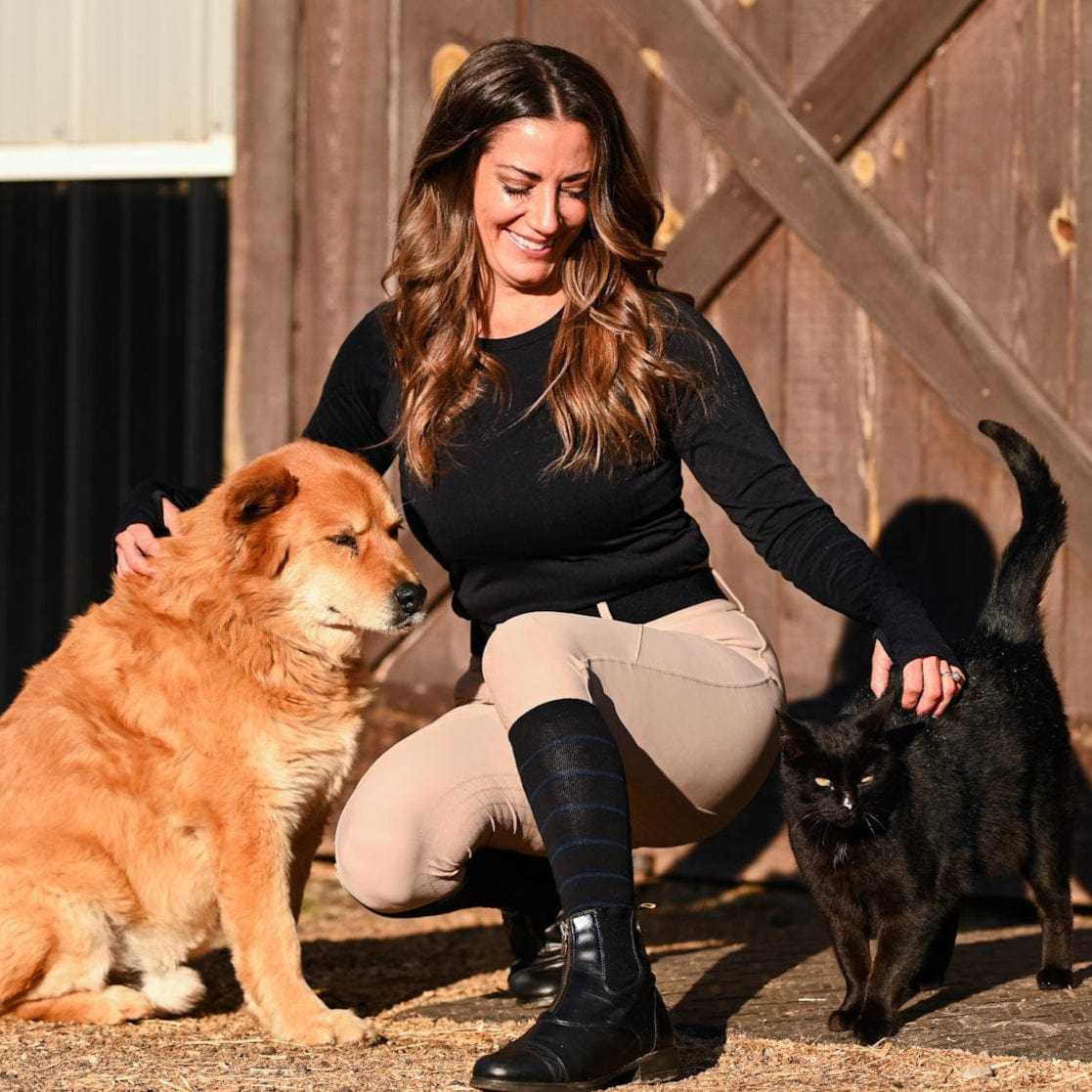 Front view of a female model wearing the black with navy stripe Dreamers & Schemers Simple Stripe Knit Boot Socks while crouching down to pet a dog and cat