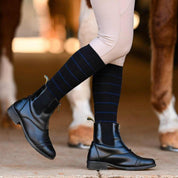 Side view of a model wearing the black with navy stripe Dreamers & Schemers Simple Stripe Knit Boot Socks while standing in front of a chestnut horse