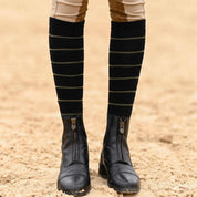 Close-up front view of a model wearing the black with sage stripe Dreamers & Schemers Simple Stripe Knit Boot Socks while standing in an arena