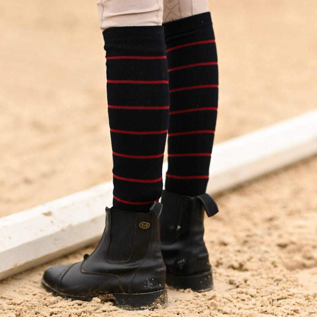 Close-up back view of a model wearing the navy with burgundy stripe Dreamers & Schemers Simple Stripe Knit Boot Socks while standing in an arena