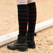 Close-up back view of a model wearing the navy with burgundy stripe Dreamers & Schemers Simple Stripe Knit Boot Socks while standing in an arena