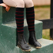 Close-up view of a model wearing the navy with burgundy stripe Dreamers & Schemers Simple Stripe Knit Boot Socks while sitting on a green mounting block