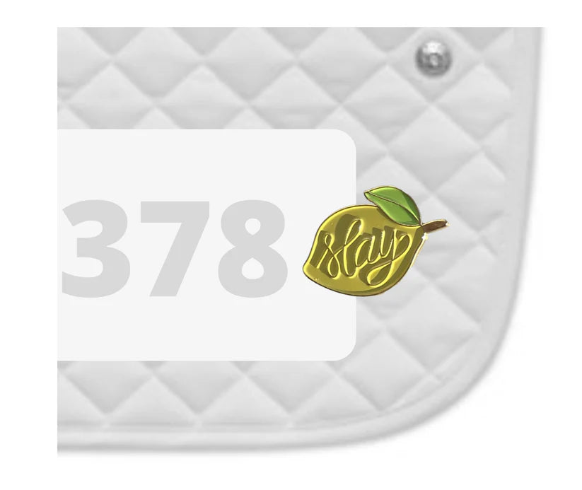 Side view of a white pad with numbers 378 and a Slay Lemon Dubois Cheval Number Pin Charm on a white background