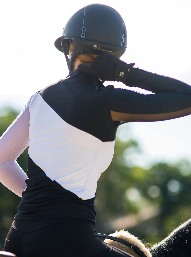 Back view of a female model wearing the black and white Criniere Sophie Stride & Conquer Schooling Shirt while riding a horse