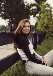 Side view of a female model wearing the black and white Criniere Sophie Stride & Conquer Schooling Shirt while sitting up against a fence