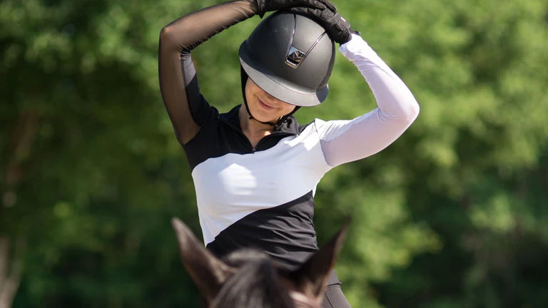Front view of a female model wearing the black and white Criniere Sophie Stride & Conquer Schooling Shirt while riding a horse