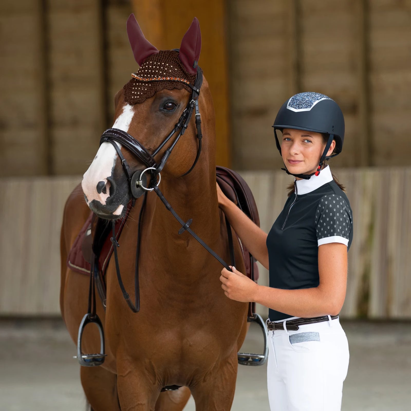 Woman in an indoor arena standing next to a chestnut horse wearing the Horze Clermont Ergonomic Crystal Bridle in brown