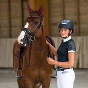 Woman in an indoor arena standing next to a chestnut horse wearing the Horze Clermont Ergonomic Crystal Bridle in brown