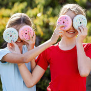 View of 2 young female models holding Dreamers and Schemers Donut Tack Cleaning Sponges over each other's eyes