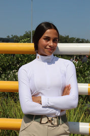 Front view of a female model wearing the white Criniere Monique The Winner's Edge Mesh Show Shirt while standing in front of a horse jump