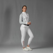 Full body front view of a model wearing the Equinavia Sara Womens Perforated Long Sleeved Show Shirt in light blue and white, white breeches, and white sneakers on a gray background