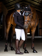 Rider standing beside a tacked up horse wearing LeMieux Acoustic Pro Fly Hood in black a stable