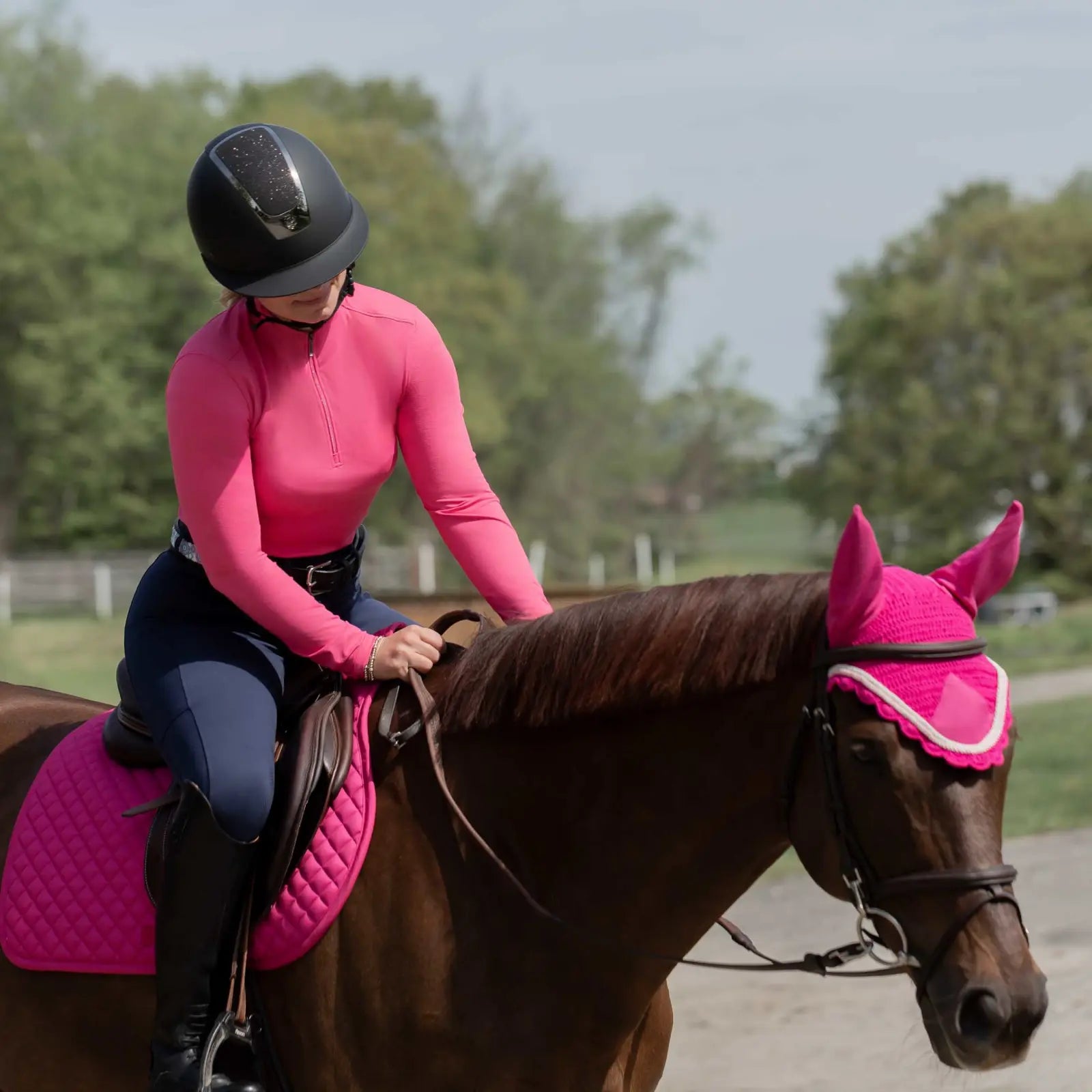 Front view of a woman wearing thethe Equinavia Kari Womens Long Sleeve Sun Shirt with NordicAir Tech in pink while riding a horse outdoors