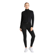 Full body front view of a model wearing the Horze Viveka Womens Perforated Training Jacket in black, black breeches, and white sneakers on a white background