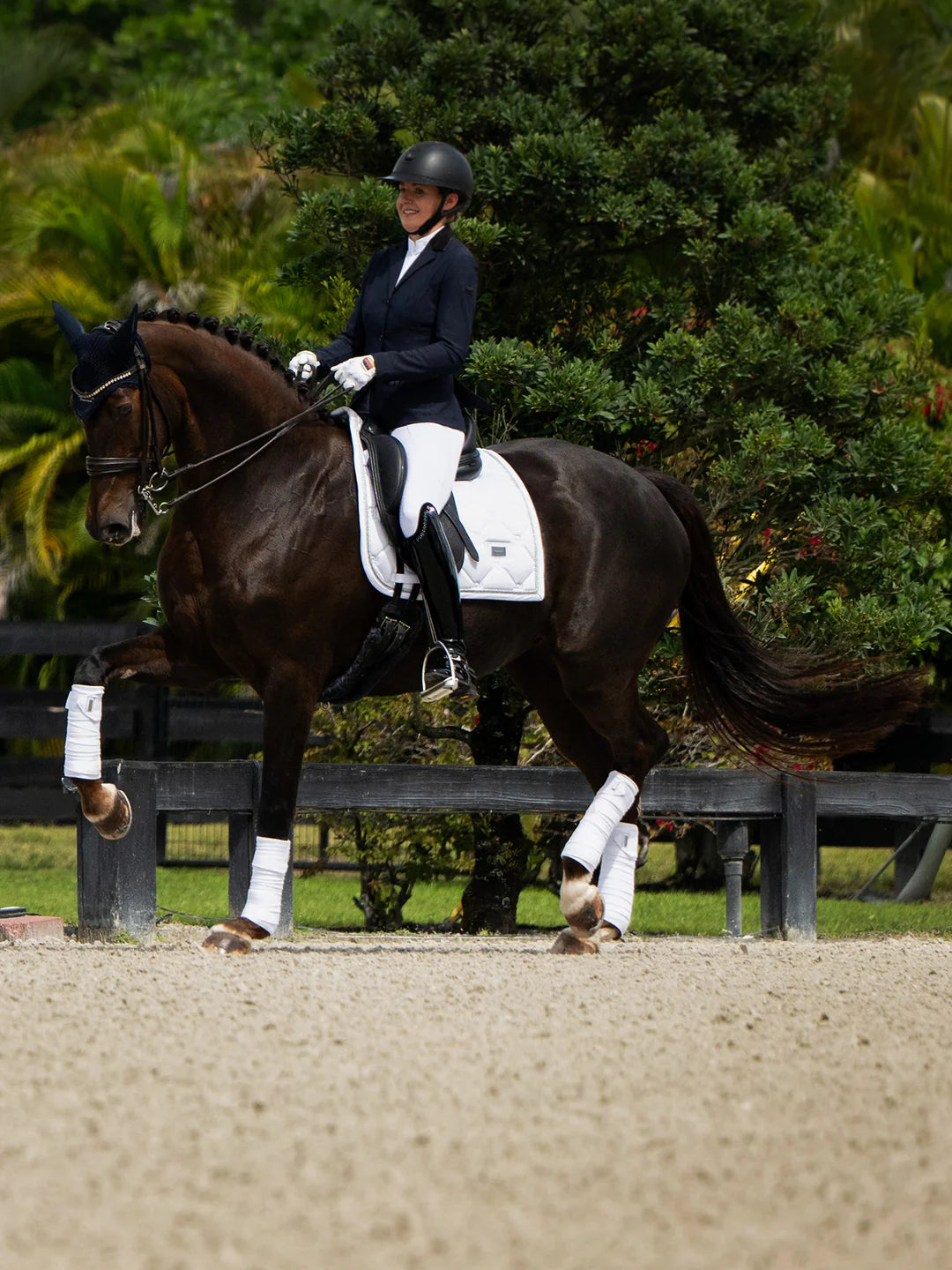 Side view of a female model riding a dark colored horse with a silver Equestrian Stockholm White Perfection Dressage Pad