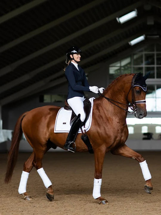 Side view of a female model riding a chestnut horse with a white Equestrian Stockholm White Perfection Dressage Pad