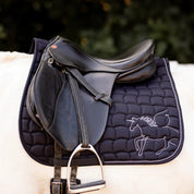 Side view of the black Horze Pegasus Pony Saddle Pad under a brown saddle on a white horse 