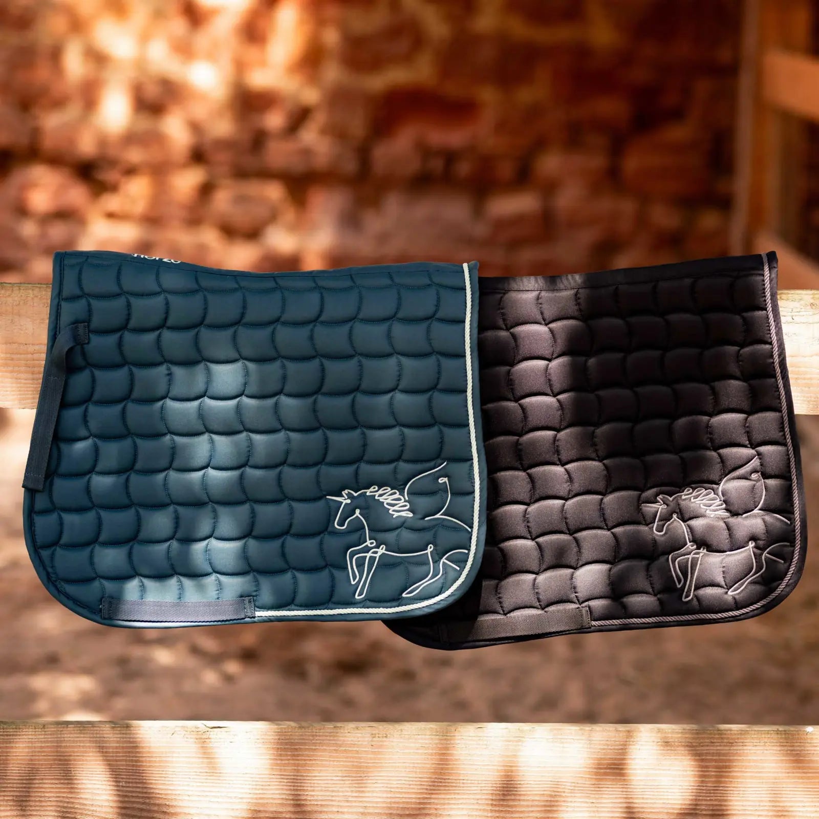 Side view of the blue and black Horze Pegasus Pony Saddle Pads draped over a brown fence in a barn