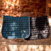 Side view of the blue and black Horze Pegasus Pony Saddle Pads draped over a brown fence in a barn
