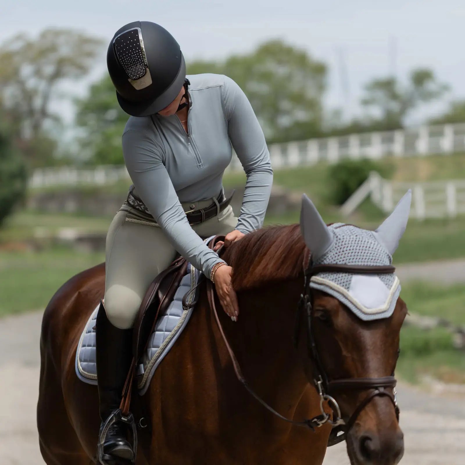 Front view of a women wearing the Equinavia Kari Womens Long Sleeve Sun Shirt with NordicAir Tech in gray while riding a horse outdoors